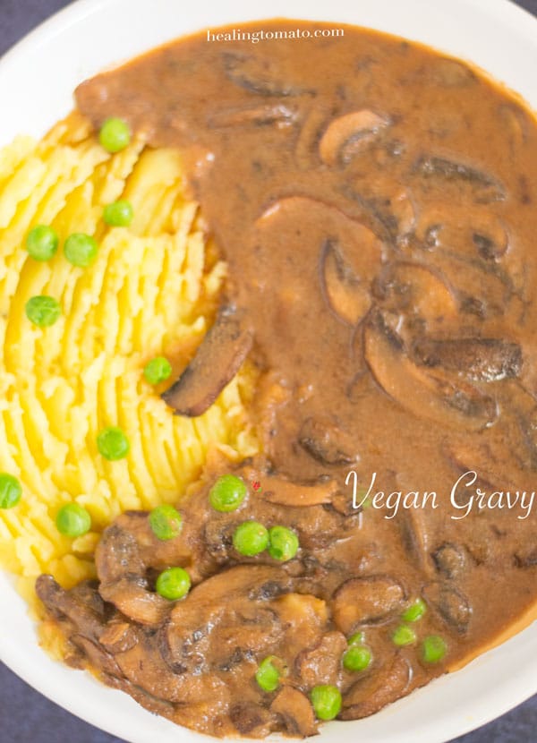Overhead and closeup view of a big while bowl filled with mashed potatoes on the left and brown vegan mushroom gravy on the right.