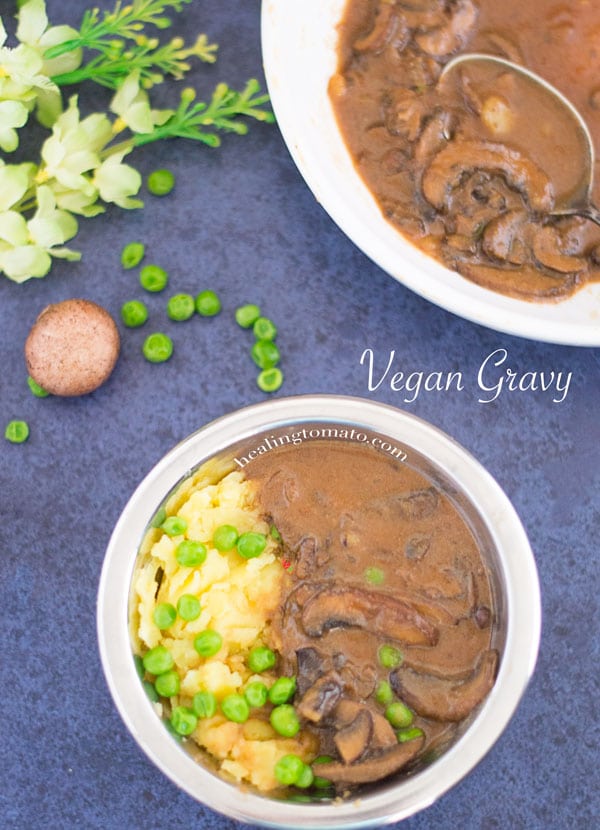 Overhead view of a small stainless steel bowl filled with mashed potatoes on the left and brown vegan mushroom gravy on the right.