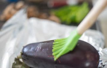 A green veggie brush on top of a small eggplant