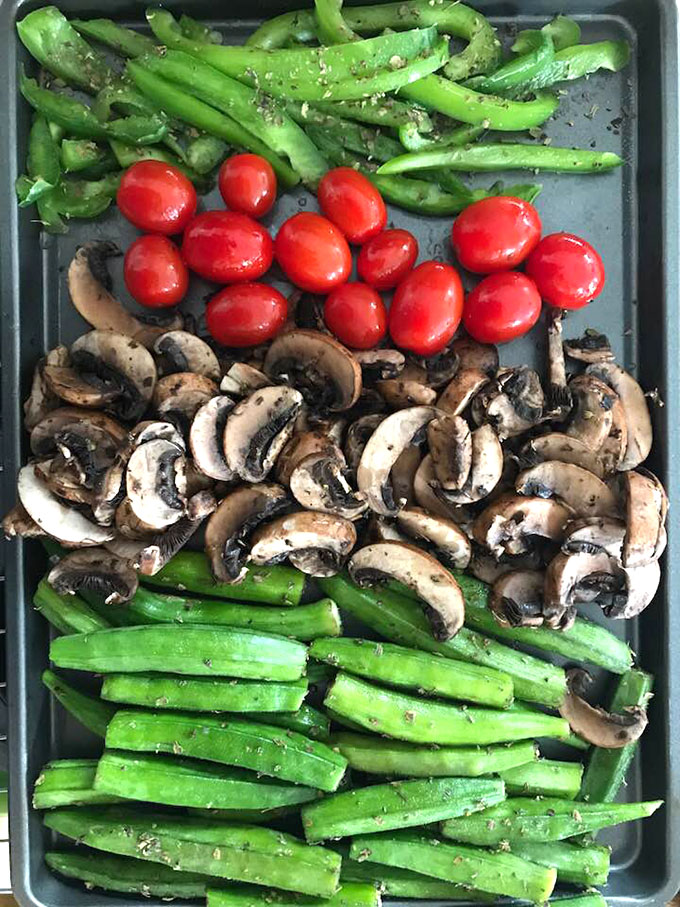 Overhead view of a baking tray filled with green bell pepper strips, cherry tomatoes, chopped mushrooms and whole okras