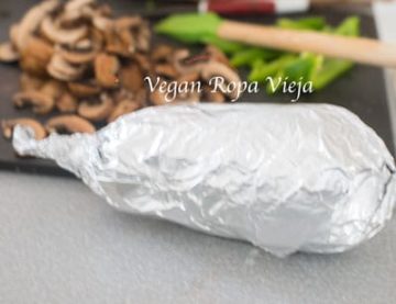 Eggplant wrapped in aluminium foil. Chopped veggies in the background