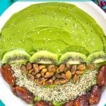 Closeup View of a Turmeric Smoothie Bowl with Green Smoothie on one half. The other half has Kiwi, Pistachios, Dates and Hemp Seeds