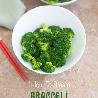 Closeup view of a white bowl of steamed broccoli with red chopsticks next to it