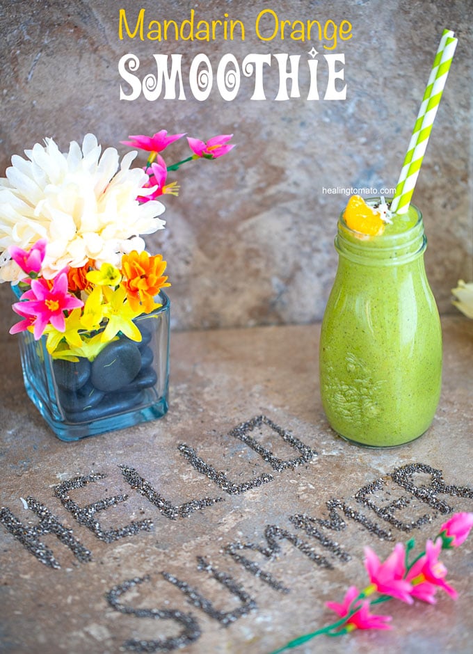 Overhead veiw of a brown tile with "Hello Summer" written out in chia seeds and a glass bottle with green smoothie on the side and a glass flower vase on the top left