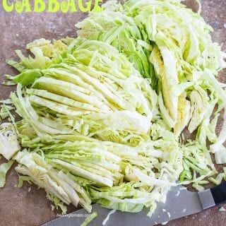 A whole cabbage cut into long, thin strips with a santoku knife next to it - How to cut cabbage