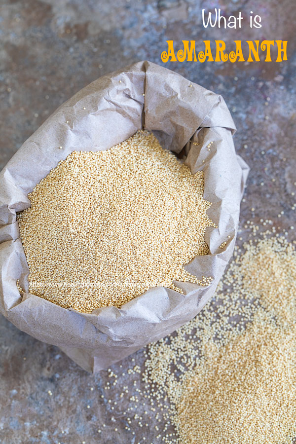 Overhead view of A small brown bag with sides folded down and filled wil amaranth grain. Its next to a small mound of amaranth grain