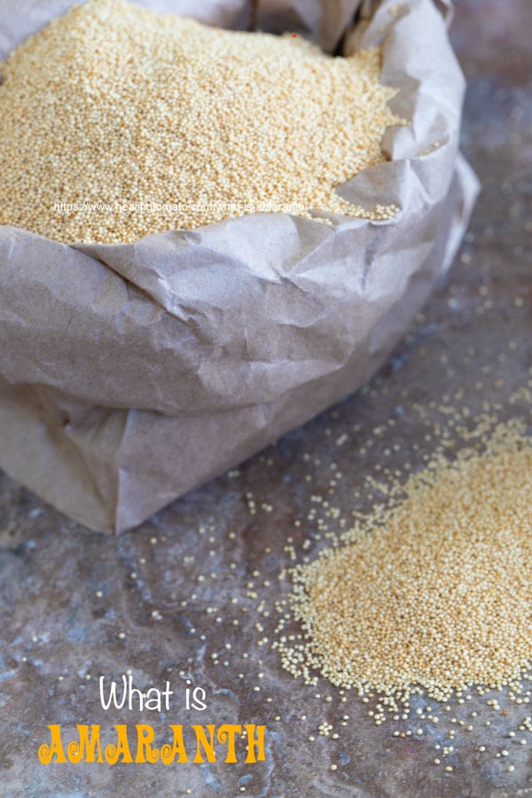 A small brown bag with sides folded down and filled wil amaranth grain. Its next to a small mound of amaranth grain