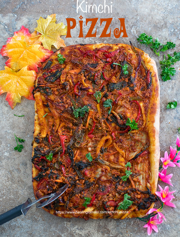 Overhead view of a whole kimchi pizza with a pizza cutter on the side