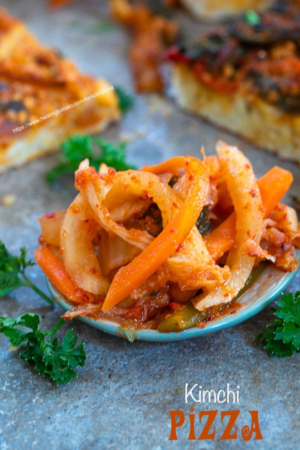 Front view of kimchi on a plate with Kimchi pizza pieces in the back