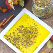 Overhead view of a white plate with Greek seasoning mix surrounded by Autumn leaves and a jar of Greek Seasoning mix