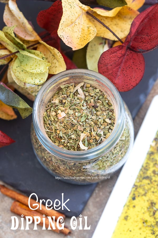 Overhead view of a glass jar filled with Greek Seasoning Mix and surrounded by Autumn leaves and Greek dipping oil