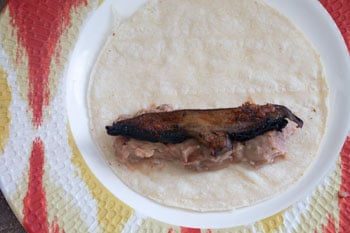 Roasted Portobello mushroom slice on refried beans on a tortilla - Vegan Taquitos