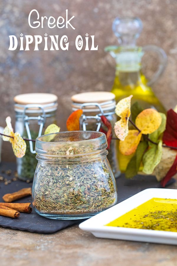 Front view of a glass jar filled with Greek Seasoning Mix and surrounded by Autumn leaves and Greek dipping oil