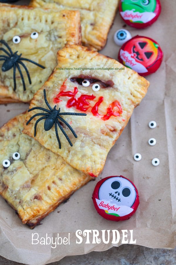 Closeup view of a Babybel strudel surrounded by Babybel cheese, candy eyes and spiders. One of the strudels has the word “HELP” written with icing - Babybel Strudel