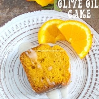 Overhead view of a slice of olive oil cake on a plate with 2 small slices of orange on the side and a rose next to the plate