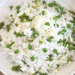 Closeup view of a white bowl filled with coconut rice and green peas.