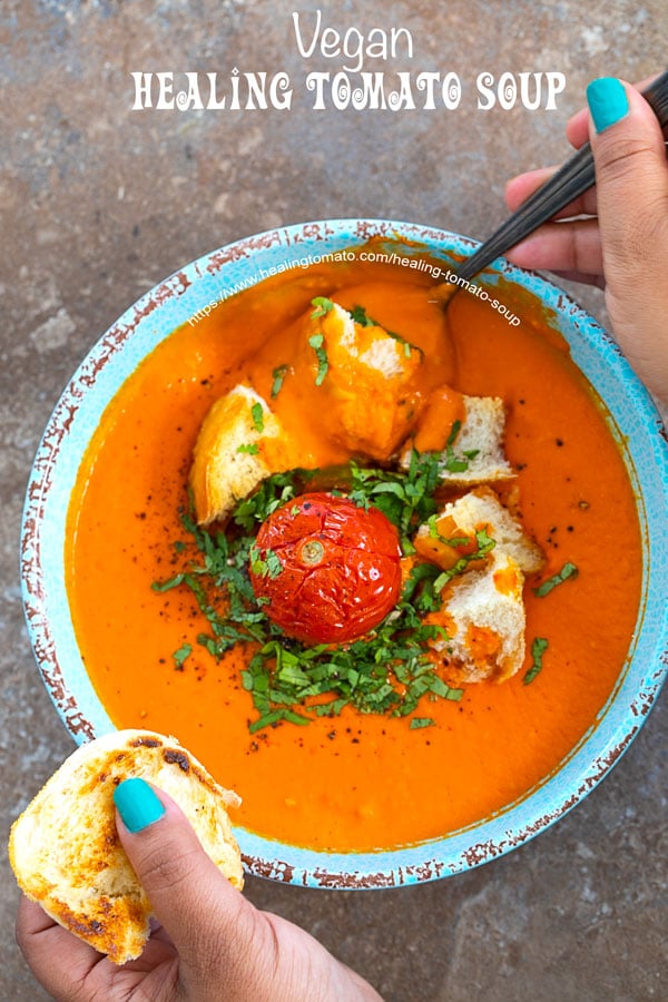 The author holding a piece of bread and digging in with the spoon into the healing tomato soup