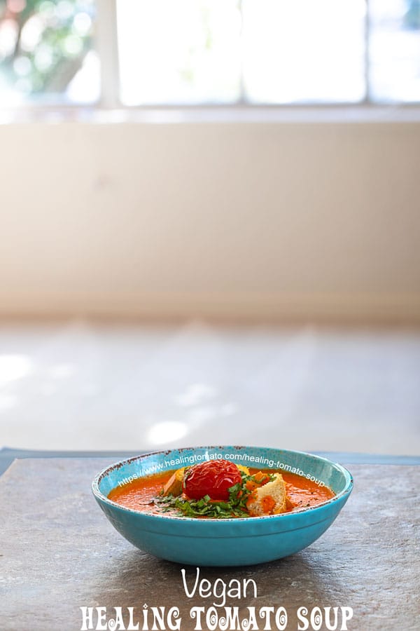 front view of tomato soup in a blue bowl with a big window behind