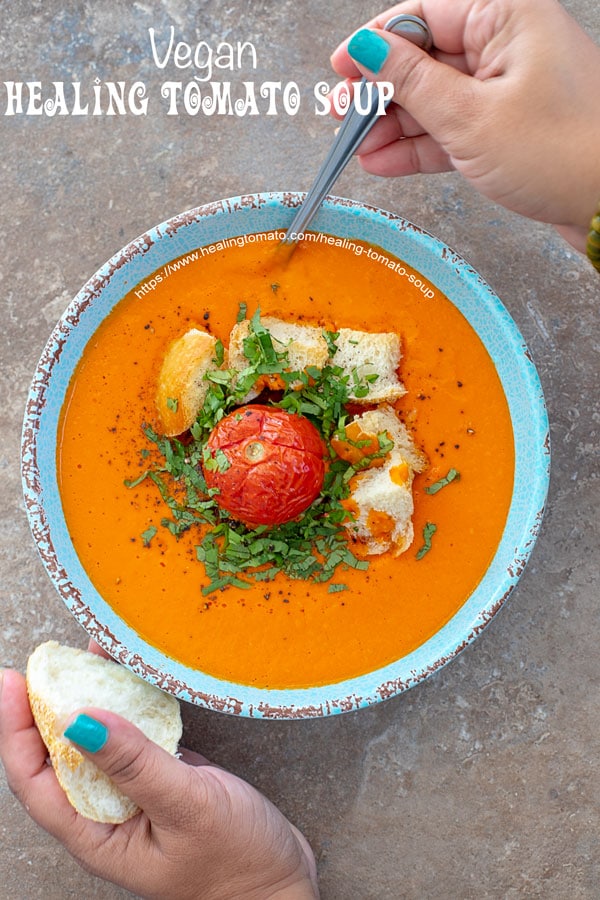 The author holding a piece of bread and digging in with the spoon into the healing tomato soup