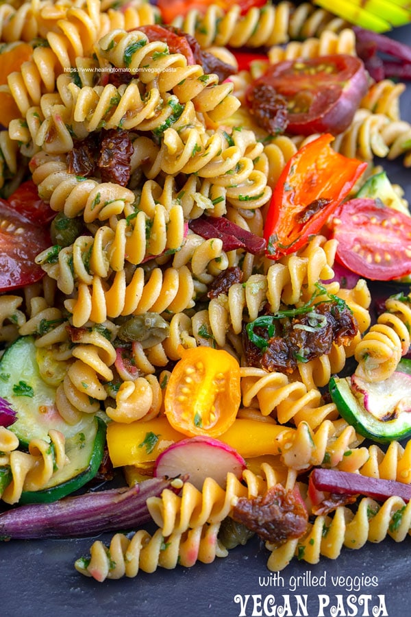 Overhead view of vegan pasta with grilled veggies on a black plate.