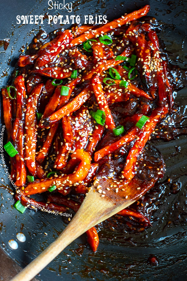 Closeup of sticky sweet potato fries in a wok with a wooden spoon