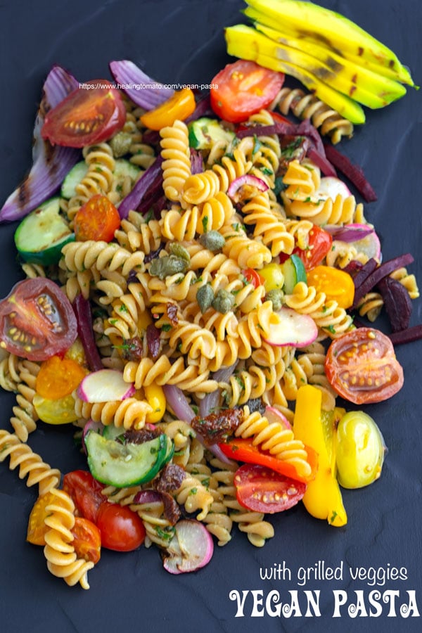 Overhead view of vegan pasta with grilled veggies on a black plate.