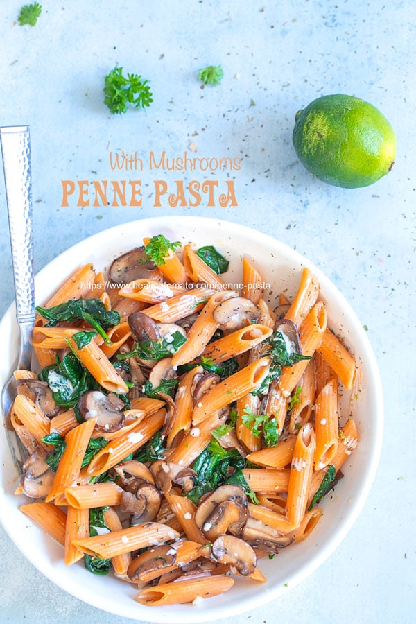Overhead view of a white bowl filled with vegan penne pasta, spinach and mushrooms