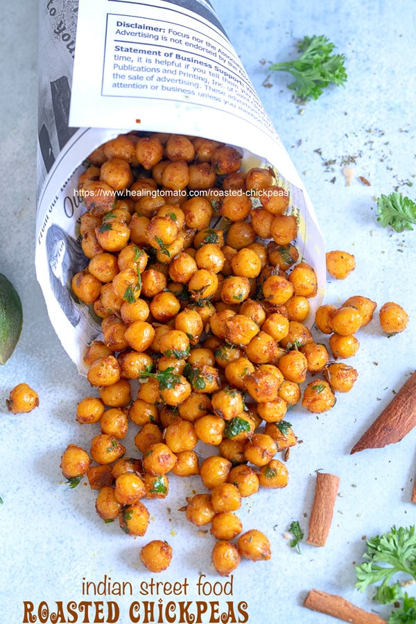 Closeup view of newspaper shaped in a cone laying flat with roasted chickpeas falling out of it - Pan fried chickpeas