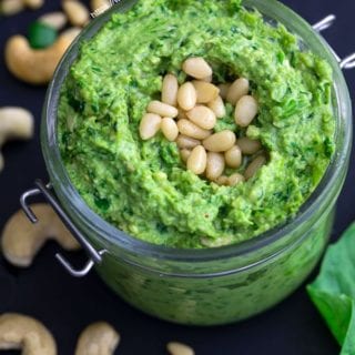 Closeup view of vegan pesto with scallions, cashews, basil and pine nuts strewn about