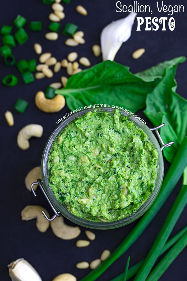 Closeup view of vegan pesto with scallions, cashews, basil and pine nuts strewn about