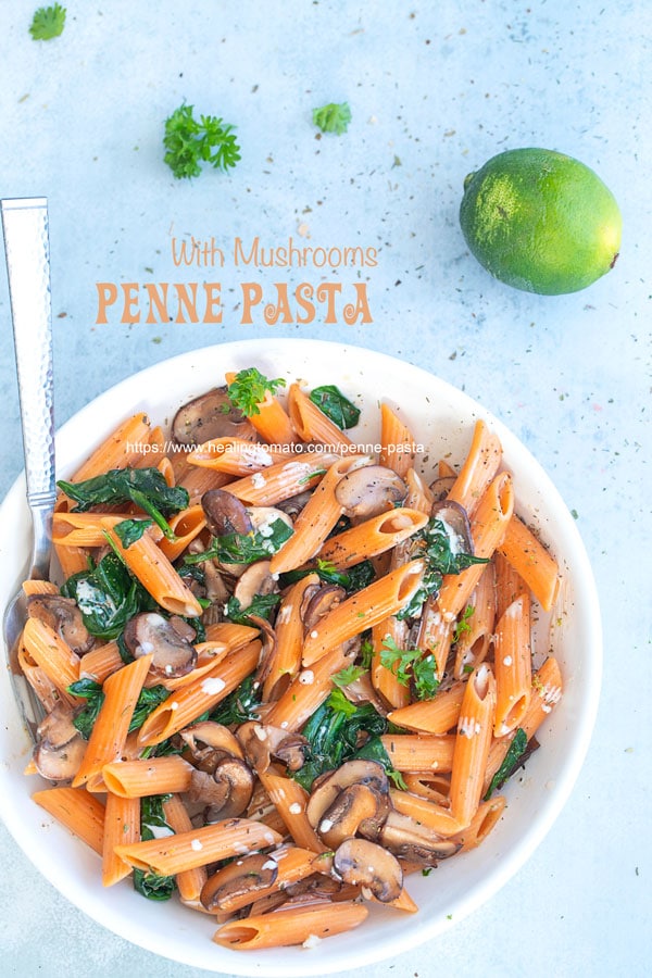 Overhead view of a white bowl filled with vegan penne pasta, spinach and mushrooms