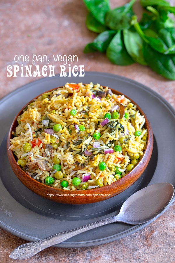 Angle view of spinach rice in a brown bowl on a rustic plate with a spoon on the side