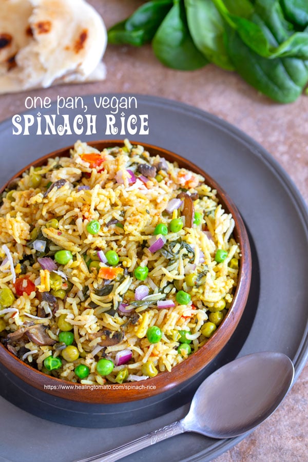 Top view of spinach rice in a brown bowl on a rustic plate with a spoon on the side