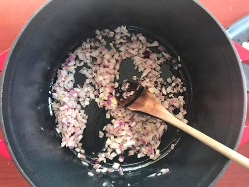 onions added to the pan and a wooden stick mixing them