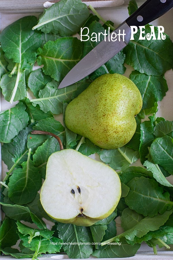 Top view of bartlett pear cut into half over kale leaves in a white tray