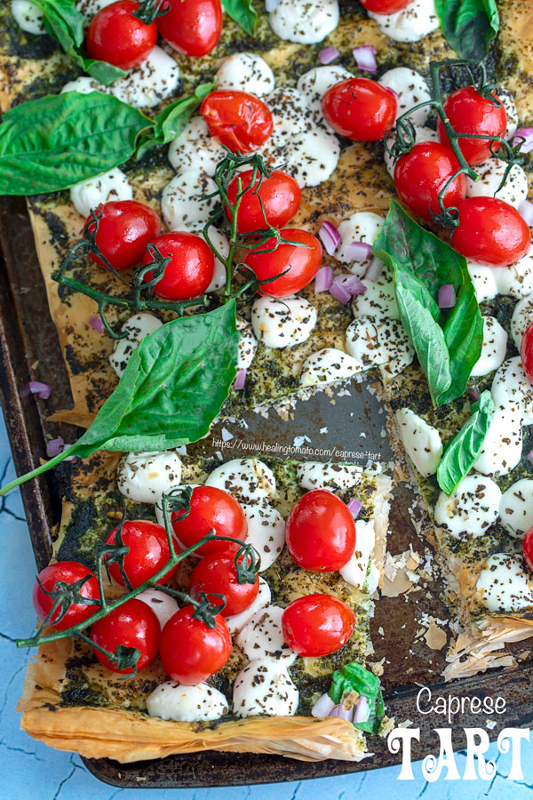 Top view of caprese tart with tomatoes on the vine, mozzarella balls and basil leaves