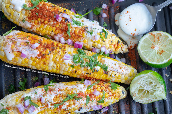 closeup view of grilled corn on the cob with lime and tofu grilling sauce on the side
