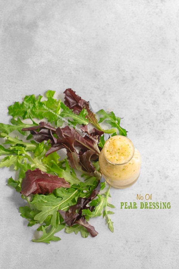 Top view of a small glass bottle filled with pear salad dressing and arugula shaped as a fan next to it