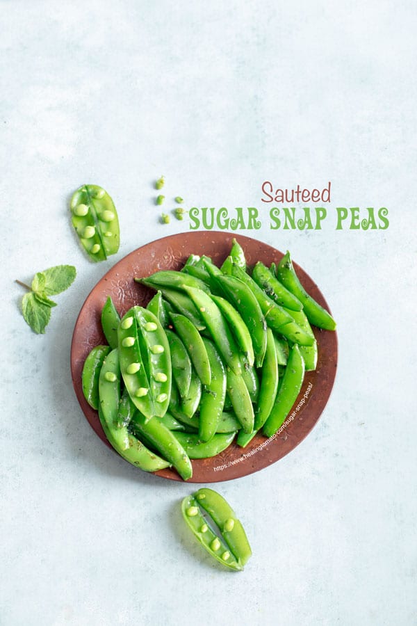 Overhead view of a brown plate filled with cooked sugar snap peas with 3 open pea pods open and a few peas on the side