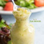 Front view of a small glass bottle filled with pear dressing with arugula salad in the background