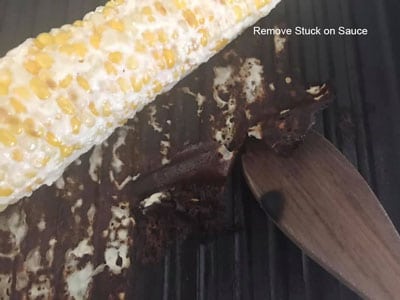 Stuck sauce placed on the side of corn being removed using a wooden spoon