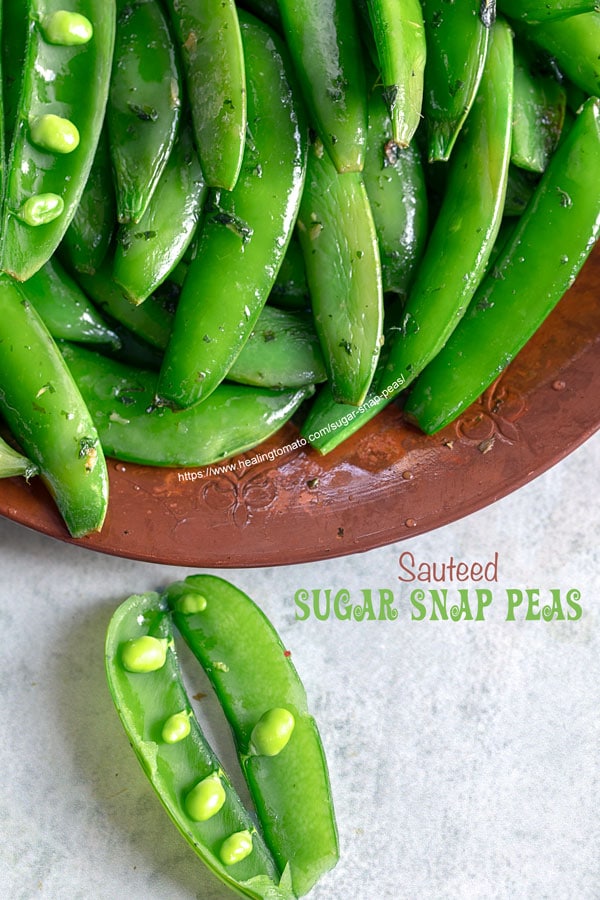 Top view of a brown plate filled with cooked sugar snap peas with 2 open pea pods