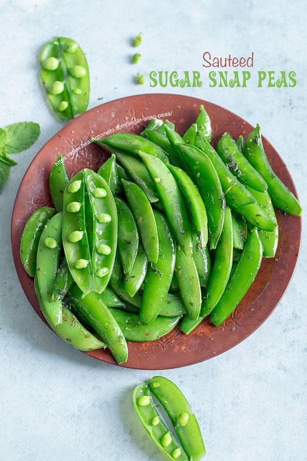 Top view of a brown plate filled with cooked sugar snap peas with 3 open pea pods open and a few peas on the side