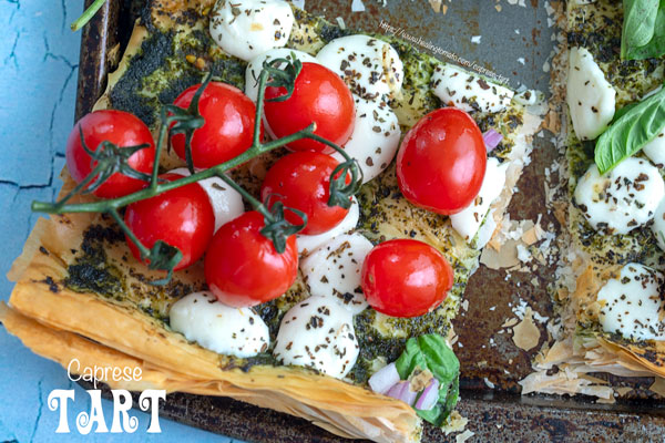 top view of cherry tomatoes on the vine on a phyllo dough tart with melted mozzarella balls