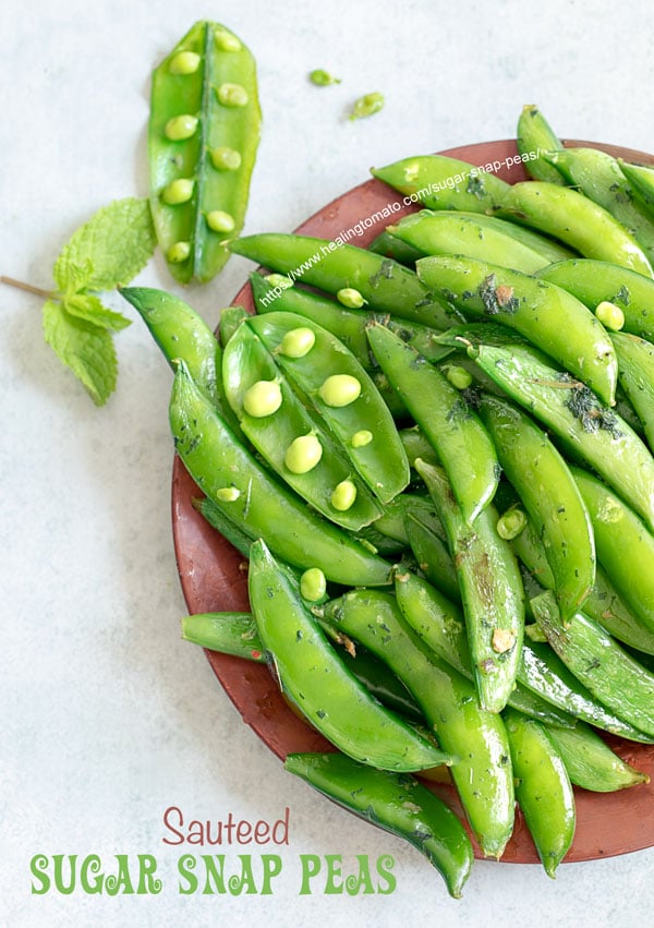 Overhead view of part of a brown plate filled with cooked sugar snap peas with 2 open pea pods open