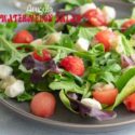 Front view of a grey plate with arugula, melon balls and mozzarella balls