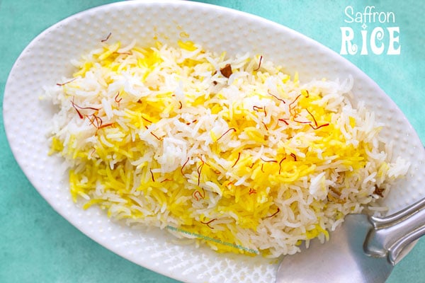 Top view of a white oval plate with saffron rice and a stainless steel rice server on the side