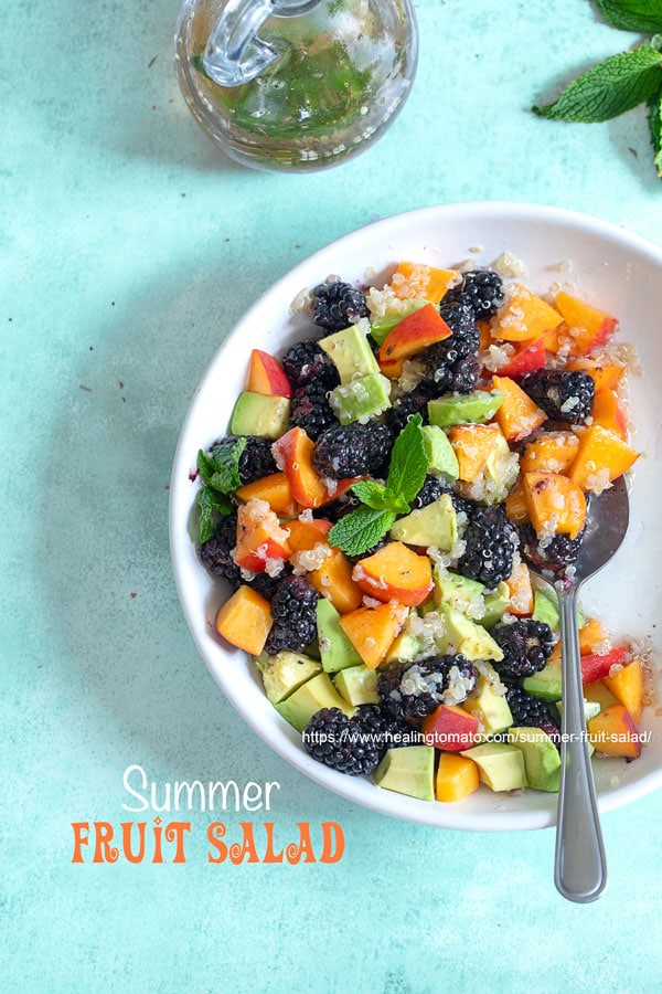 Top view of a white bowl with blackberries, peaches, avocado and quinoa.