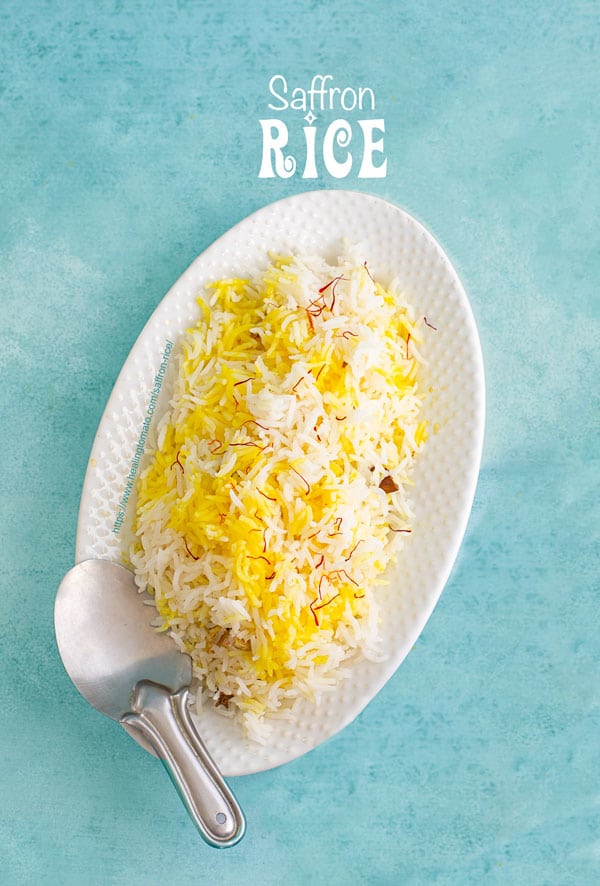 Top view of a white oval plate with saffron rice and a stainless steel rice server on the side