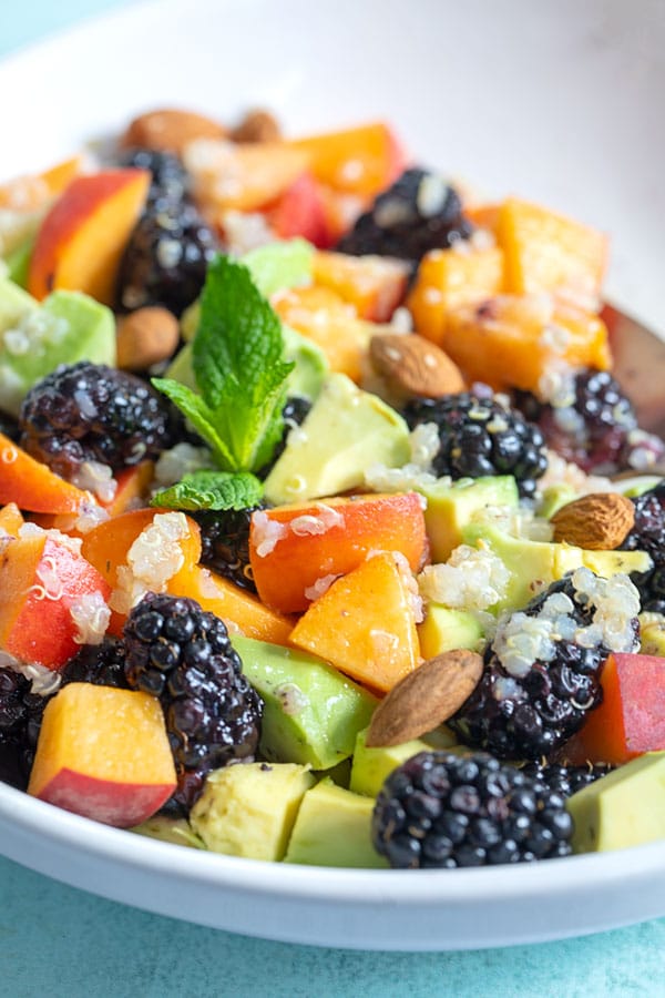 Closeup view of a white bowl with blackberries, peaches, avocado and quinoa.